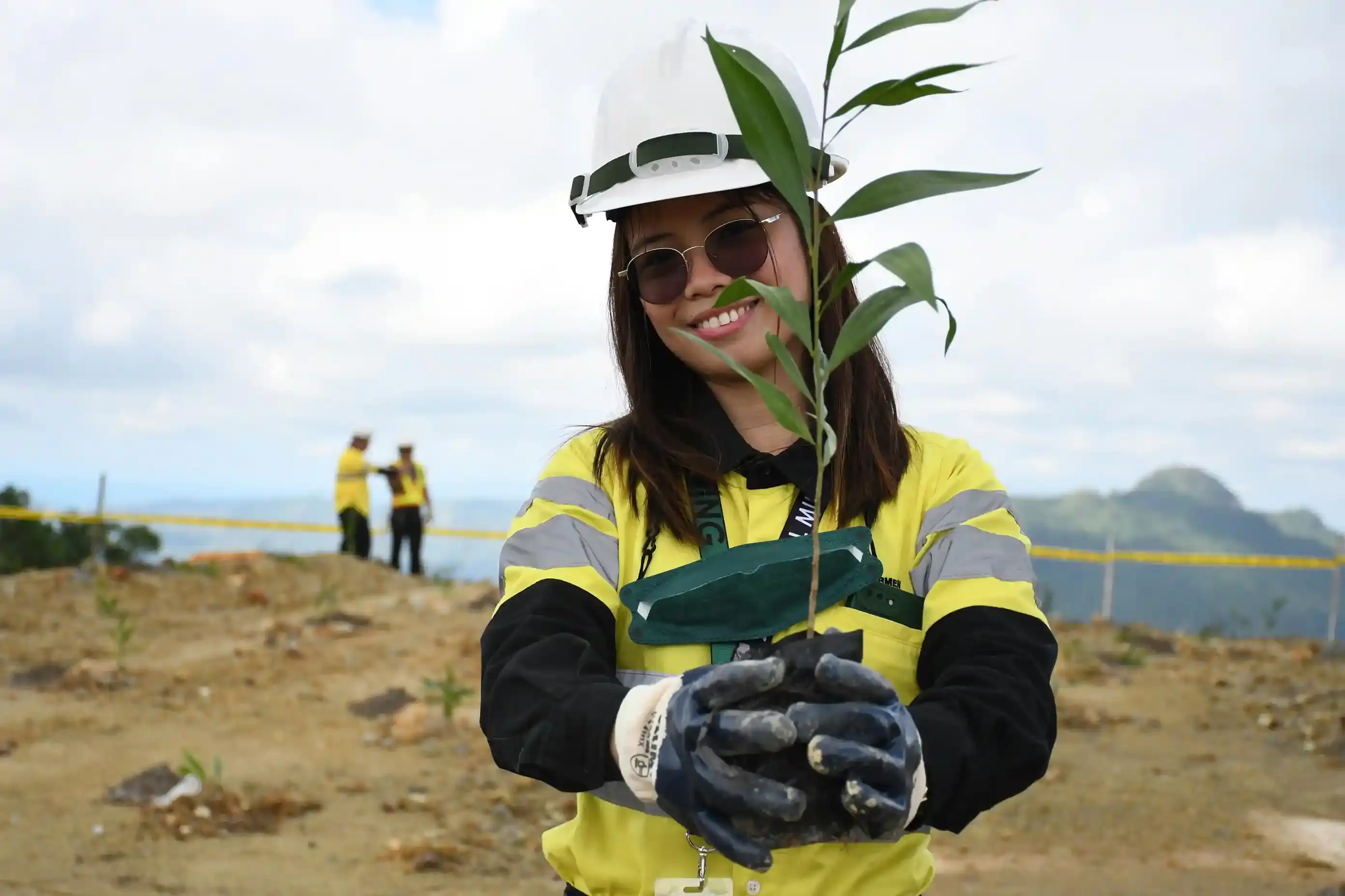 An image of a environmental worker in a hardhat holding a plant on a construction site